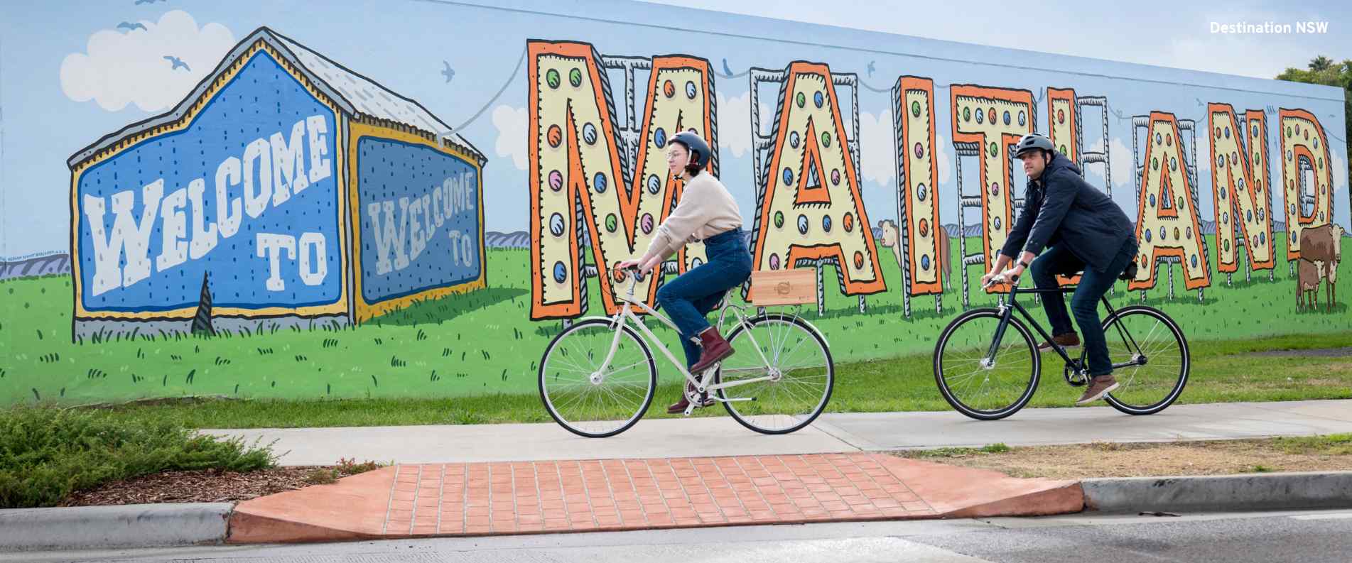 People cycling by the Welcome to Maitland sign